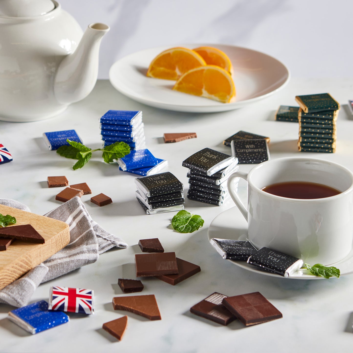 Dark Mint Chocolate Neapolitans, each piece a celebration of the rich, bold flavours of dark chocolate infused with the cool, refreshing essence of mint. Encased in elegant foil and paper wrappers that feature a sleek black background with 'with compliments' elegantly printed in silver. Packed in 2kg bulk catering boxes