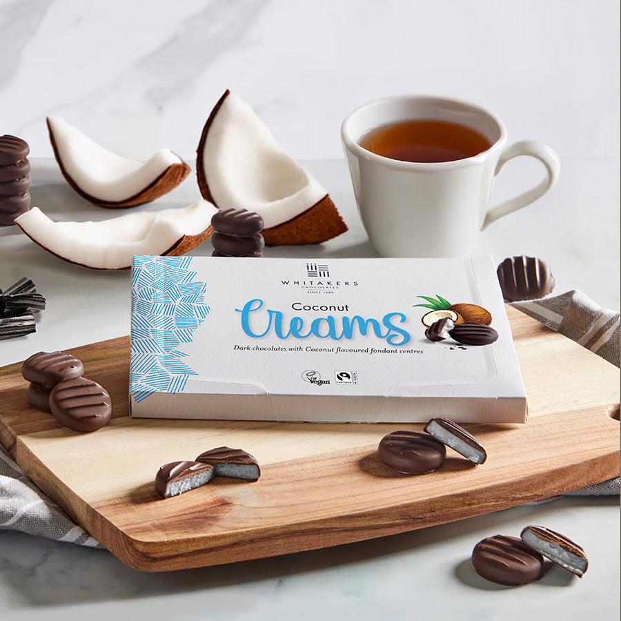 Box of Coconut Creams with a cup of tea and coconut halves on a marble surface