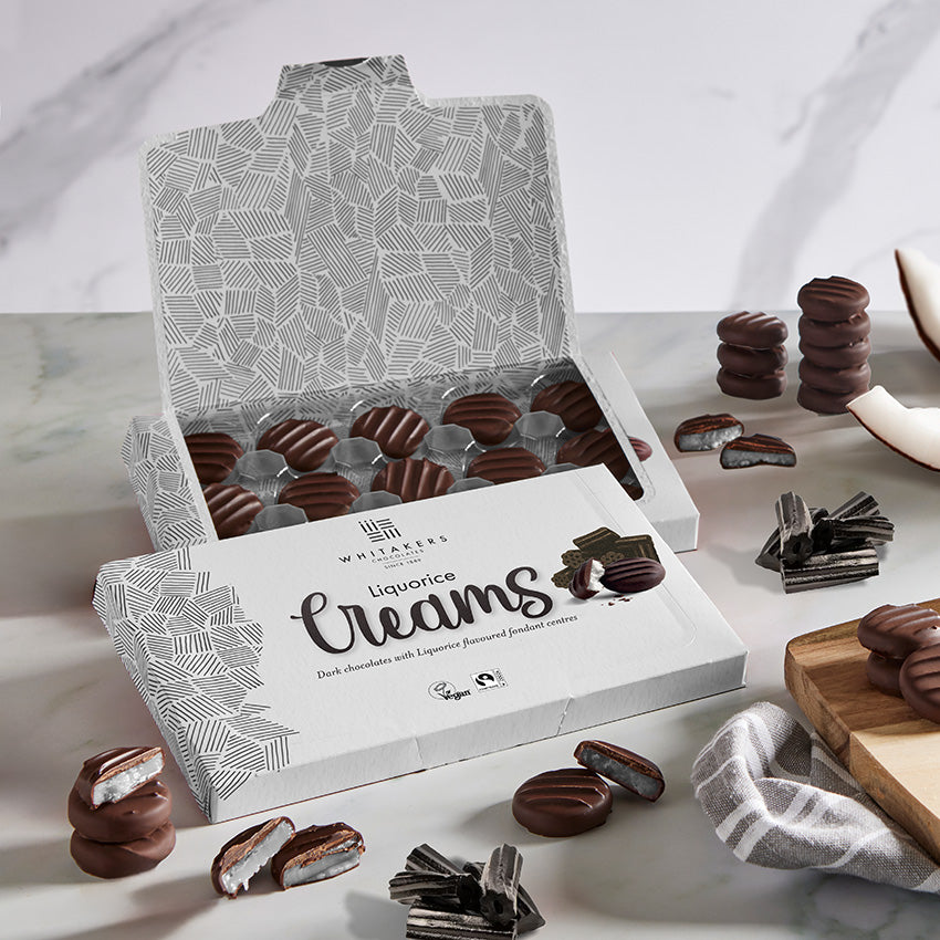 Open box of Liquorice Creams with some candies on a marble surface