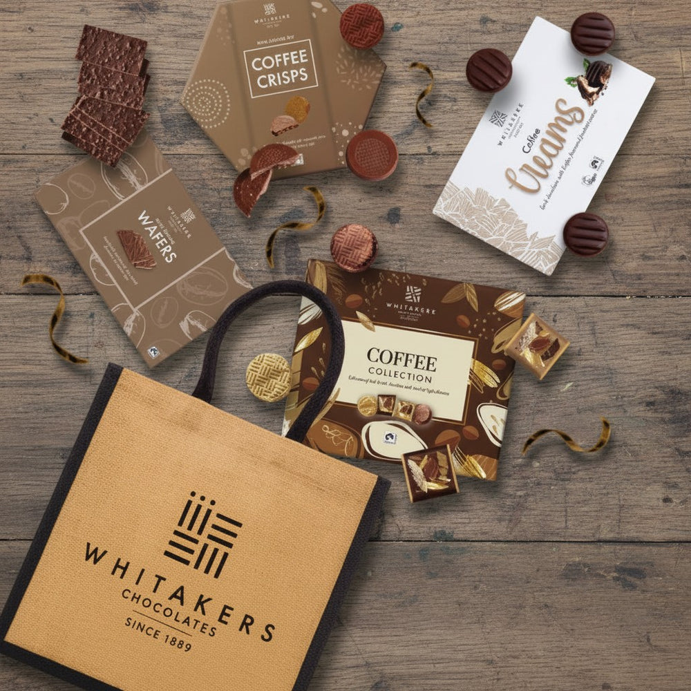 Whitakers Fairtrade coffee lovers chocolate hamper with natural tote bpg on a wooden surface with coffee crisps, coffee creams, coffee collection & coffee wafers boxes