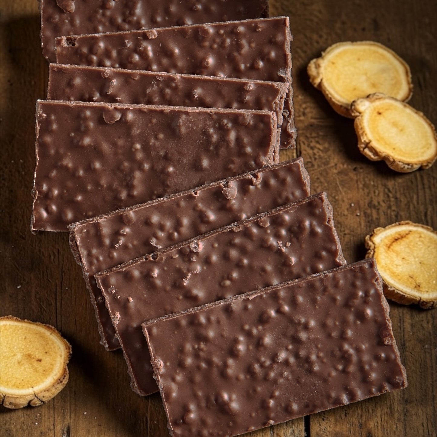 stack of dark chocolate ginger wafers on a wooden background, with ginger slices around the chocolates