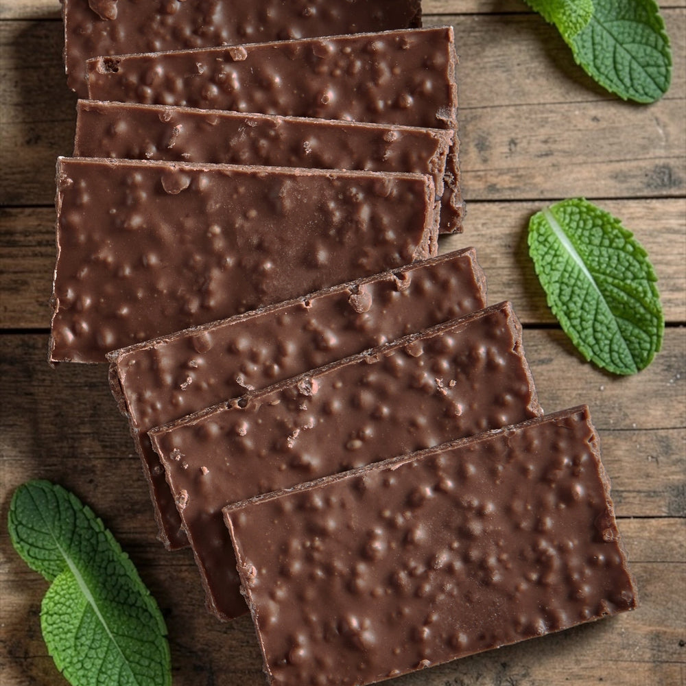 Stack of dark chocolate mint wafers on a wooden background with mint leaves scattered around the chocolates