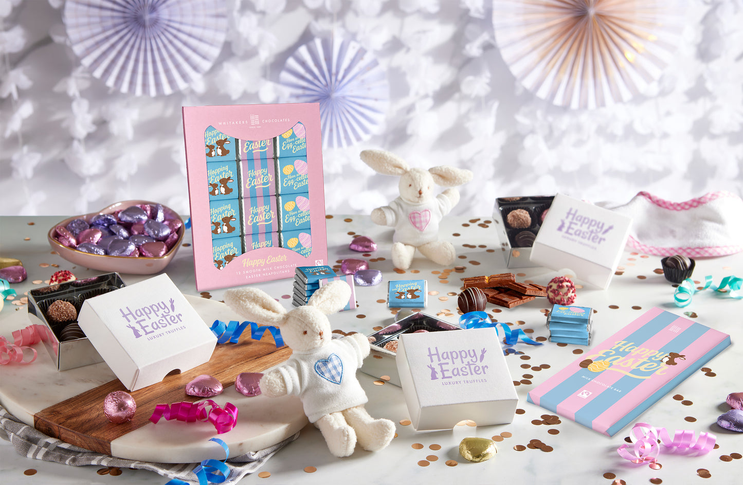 Easter-themed gift set with chocolate eggs, bunny figurines, and decorative items on a white surface.