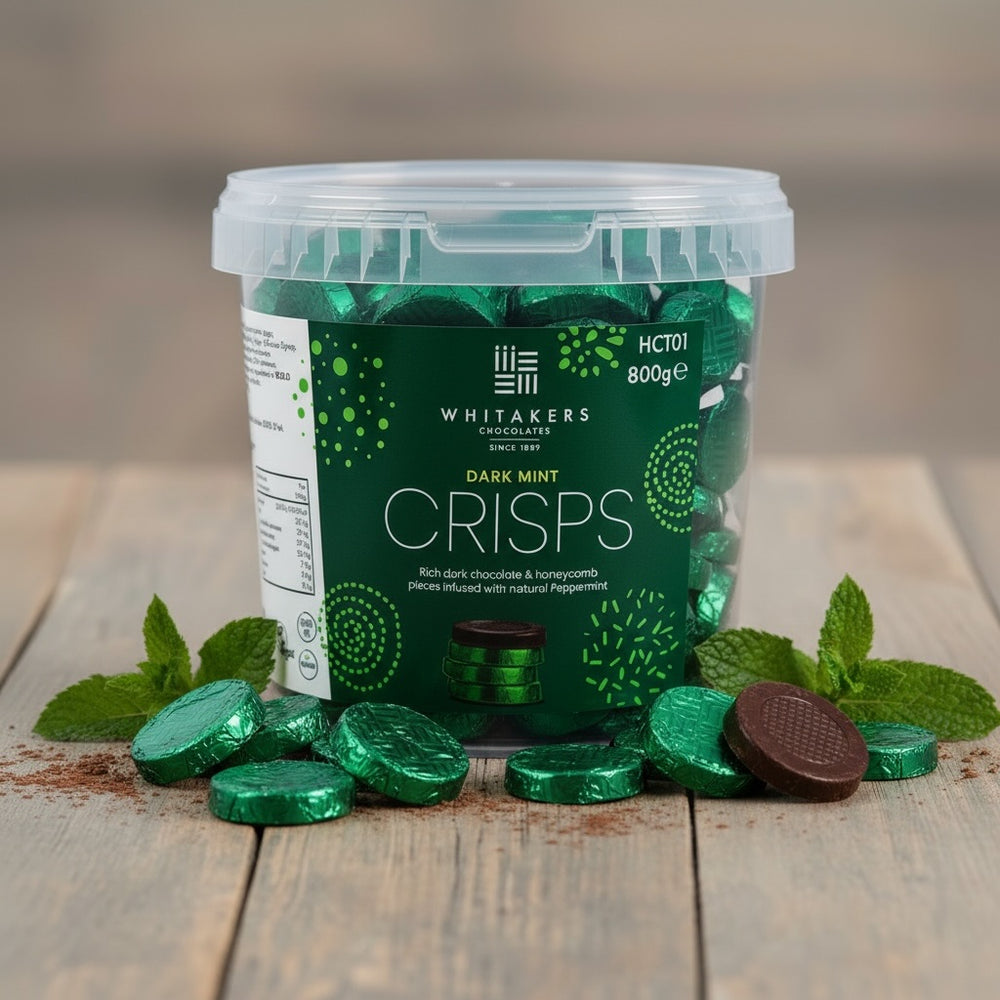 Container of Whitaker's green foiled Dark Mint Crisps on a wooden surface with mint leaves.