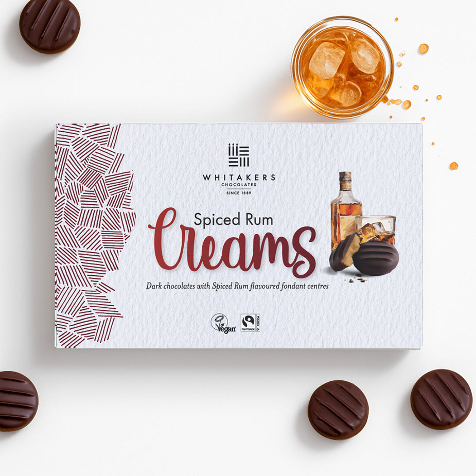 Box of Whitaker's Spiced Rum Creams with chocolates and a cocktail on a white background