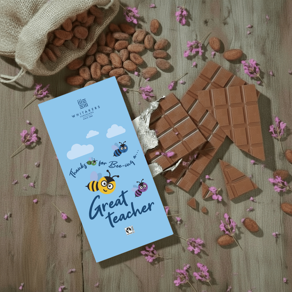 Whittaker's chocolate bar with a 'Thanks for being a great teacher' message on a wooden surface with chocolate pieces and flowers.