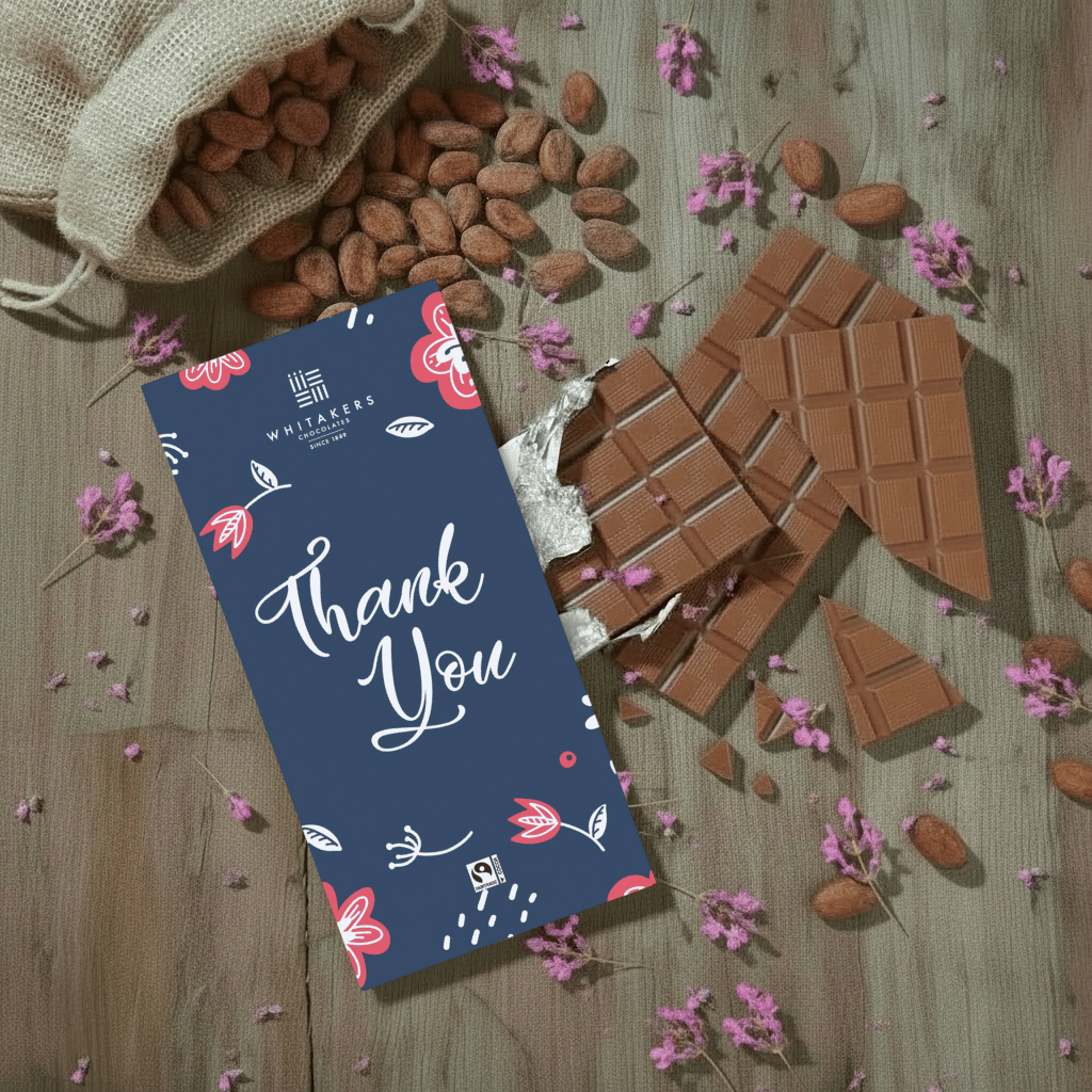 Whittaker's milk chocolate bar with a 'Thank You' card on a wooden surface with almonds and flowers.