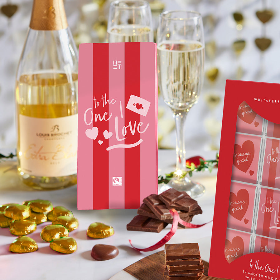 Bottle of Louis Roederer Cristal champagne, chocolate bars, and a pink gift box with 'to the one I love' text on a decorative background.