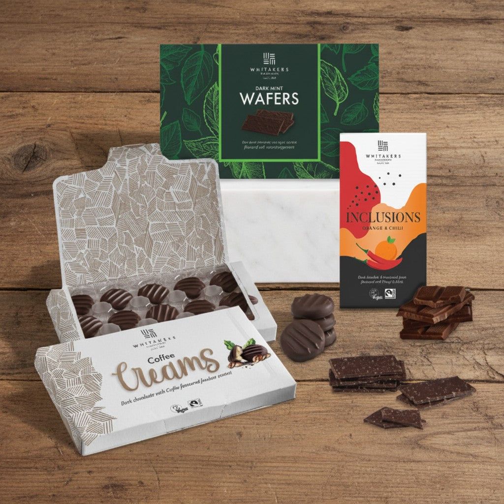 Whitakers Chocolates Assorted chocolate products including Coffee Creams, Wafers, and Inclusions chilli and orange bar on a wooden surface.