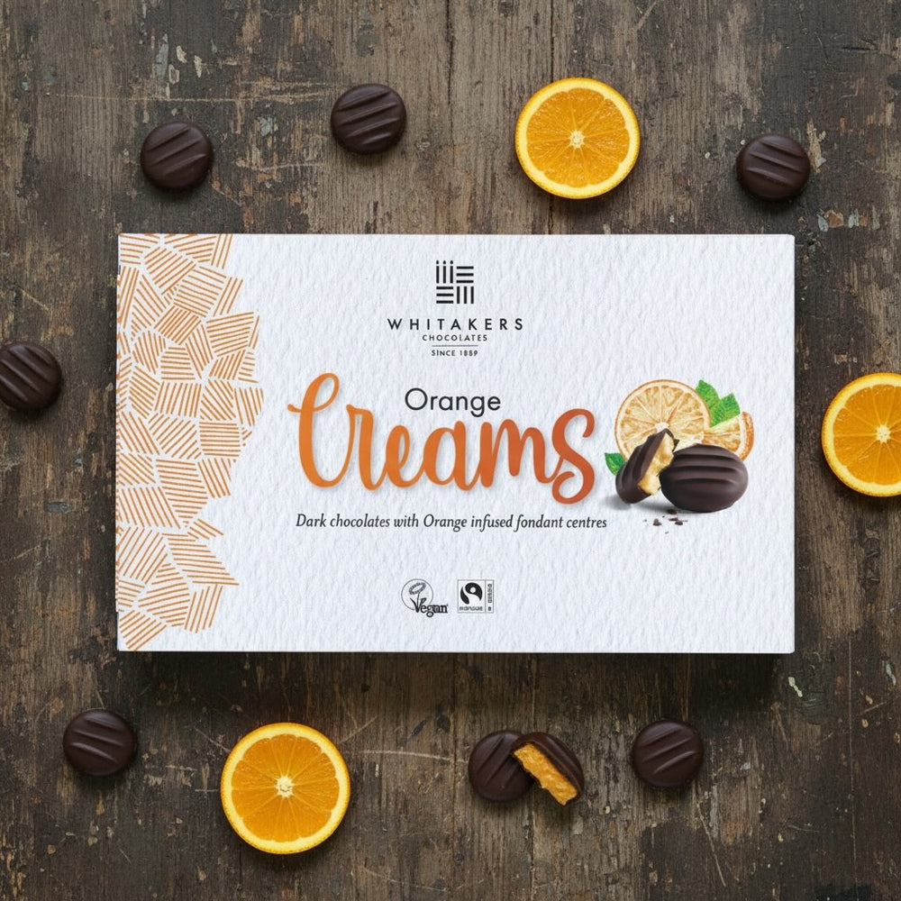 Whitaker's dark chocolate Orange Creams chocolate box on a wooden surface with oranges and chocolates.
