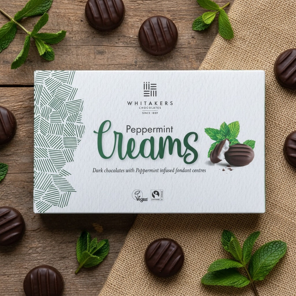 Box of Whitaker's dark chocolate Peppermint Creams chocolates on a wooden surface with mint leaves.