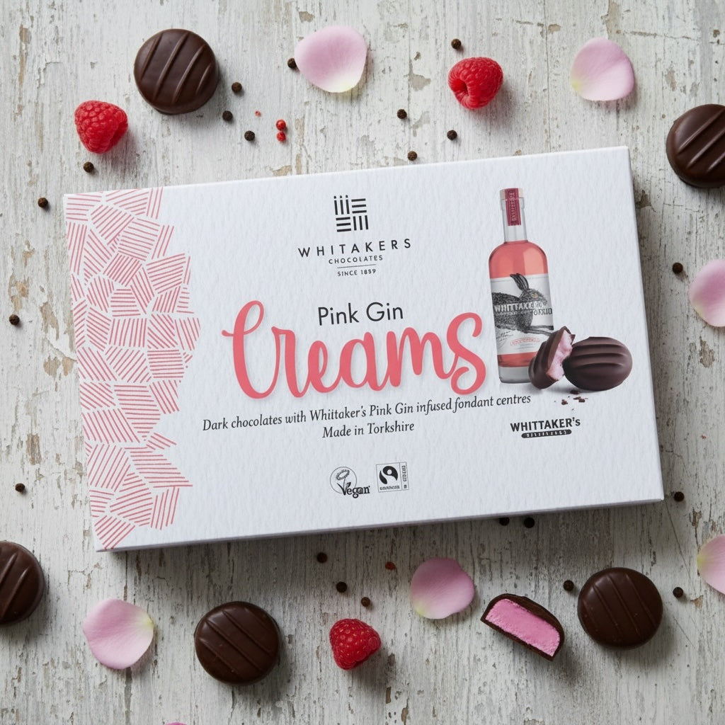 Box of Whitaker's dark chocolate Pink Gin Creams with chocolates and berries on a wooden surface