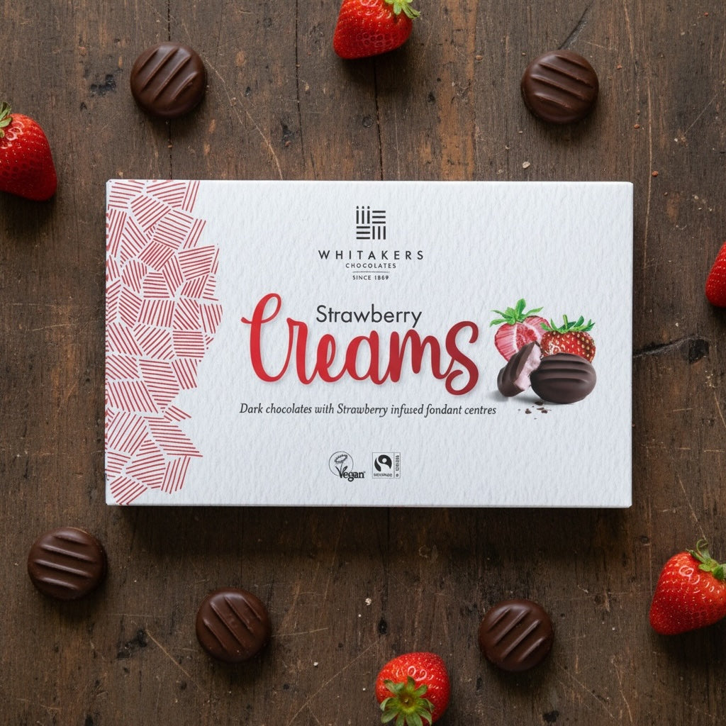 Whitaker's dark chocolate Strawberry Creams chocolate box on a wooden surface with strawberries and chocolates.
