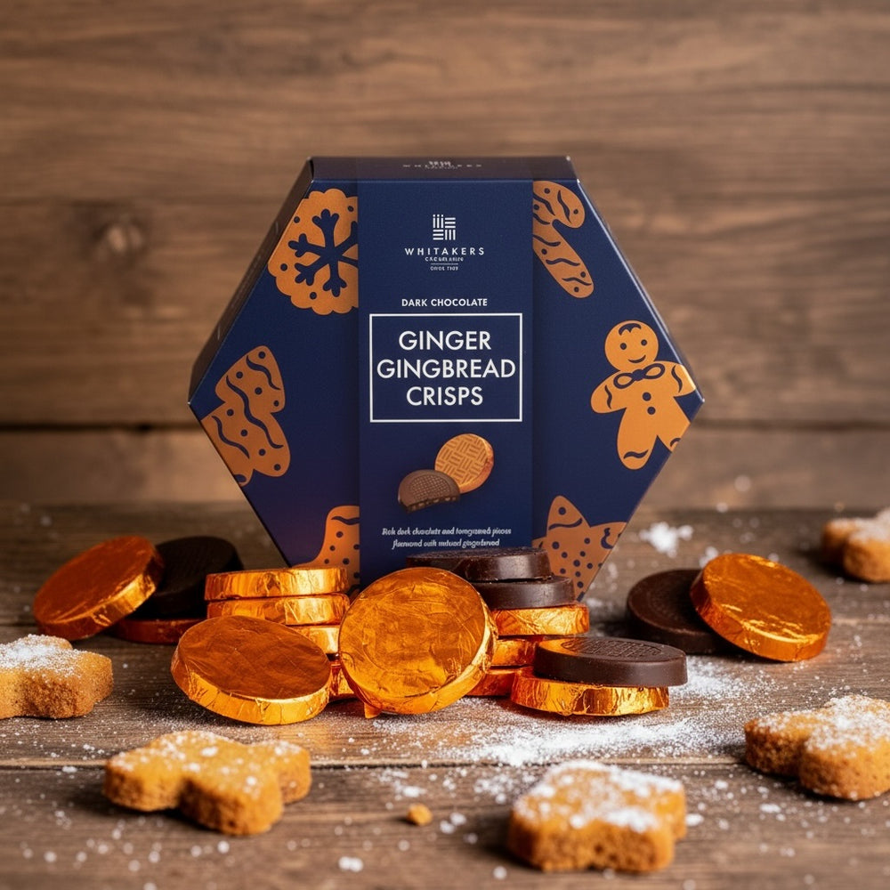 Box of Whitaker's orange foiled Ginger Gingerbread Crisps on a wooden surface with gingerbread cookies and chocolate coins.