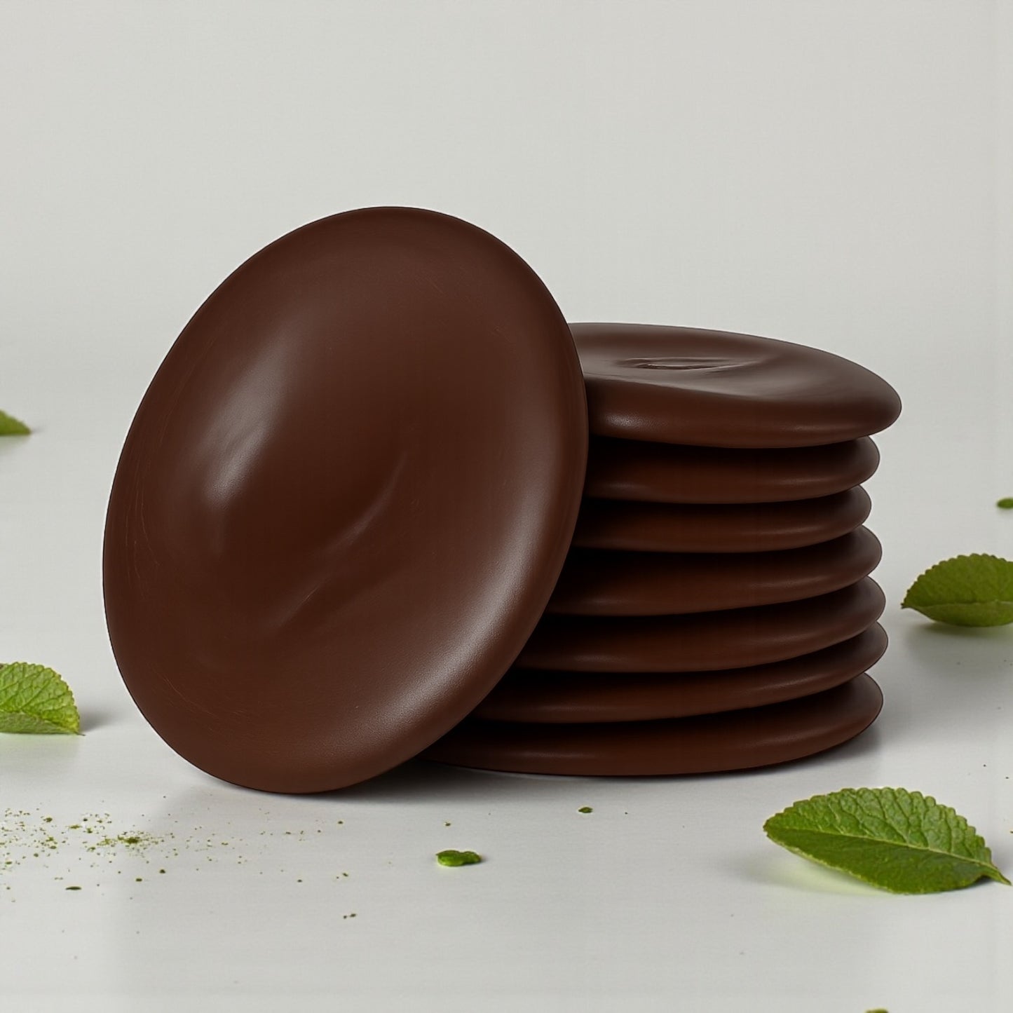 Stack of dark chocolate mint thins with mint scattered around on a white background