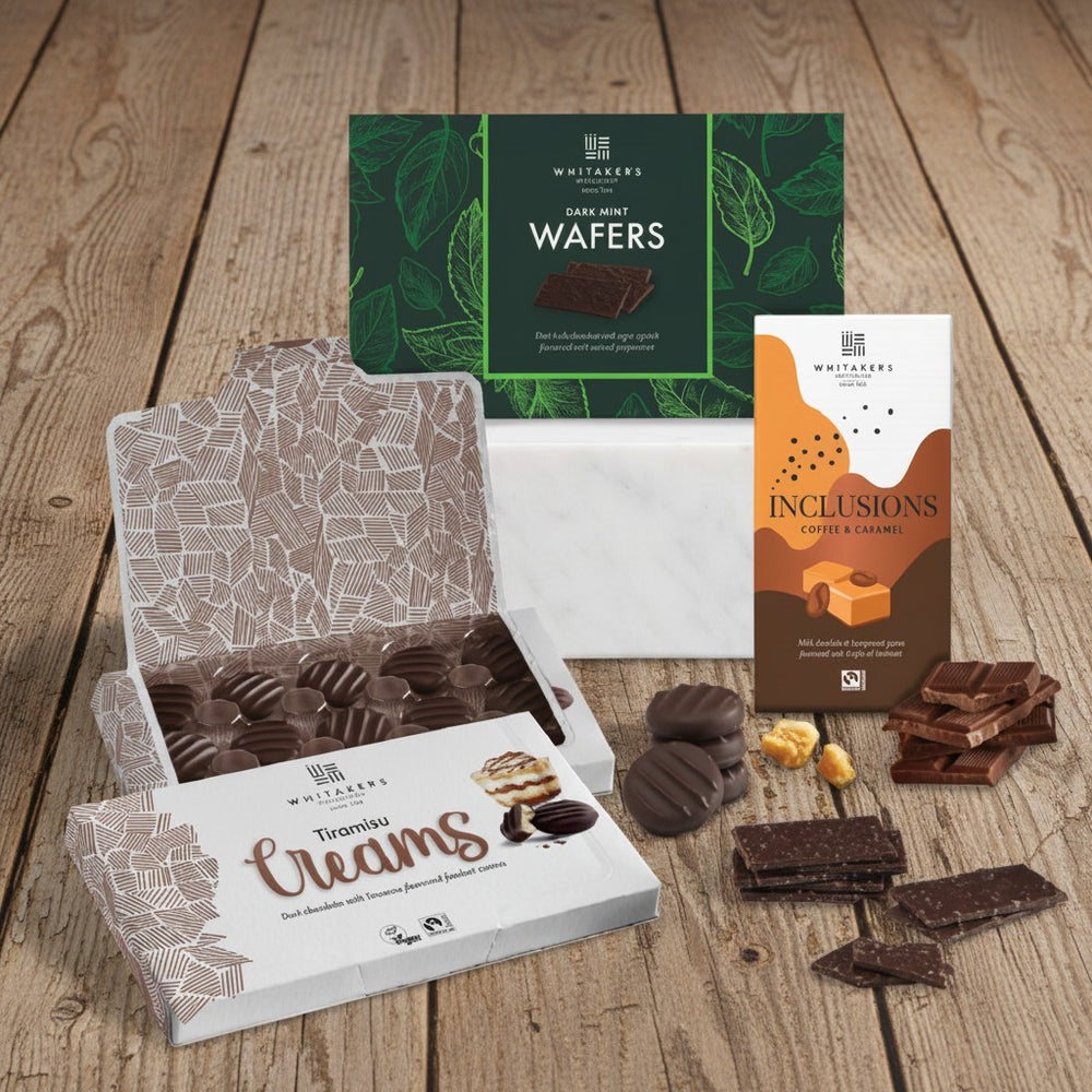 Assorted Whitakers chocolate products including 'Tiramisu Creams', 'Wafers', and 'Inclusions' on a wooden surface.