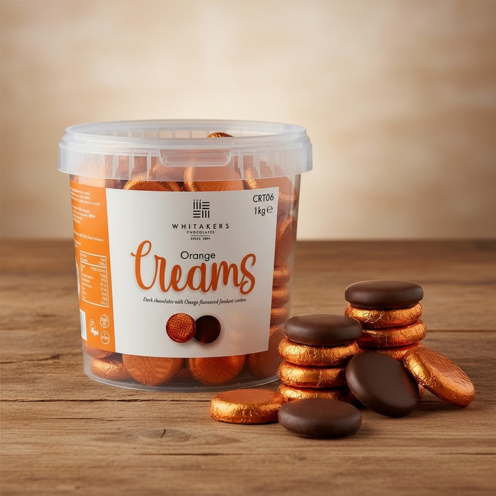 Tub of Whitakers Orange foiled dark chocolate orange creams on a wooden surface