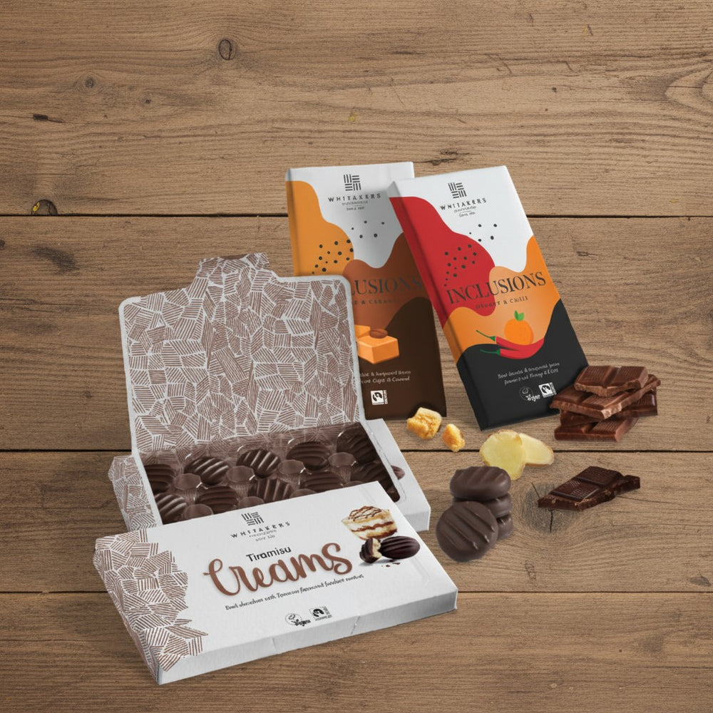Whitakers Chocolates on a rustic wooden surface. Featuring dark chocolate tiramisu creams, milk coffee & caramel chocolate bar and dark chocolate chilli & orange bar.