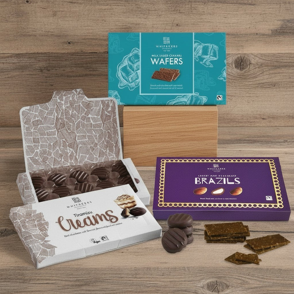 Whitakers Chocolates Assorted Fairtrade chocolates, including milk salted caramel wafers, tiramisu fondant creams, and milk chocolate Brazils on a wooden surface